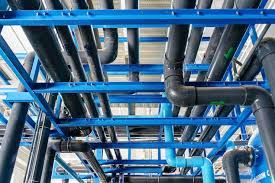 A complex industrial piping system composed of black and blue pipes supported by a blue metal framework, featuring multiple joints and connectors in a facility likely used for water treatment, chemical processing, or HVAC operations.