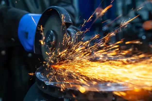 metal fabrication in qatar-markline trading & contracting Close-up of a person using an angle grinder on metal, with bright sparks flying and a blue protective glove visible, highlighting active metalworking in a workshop setting.
