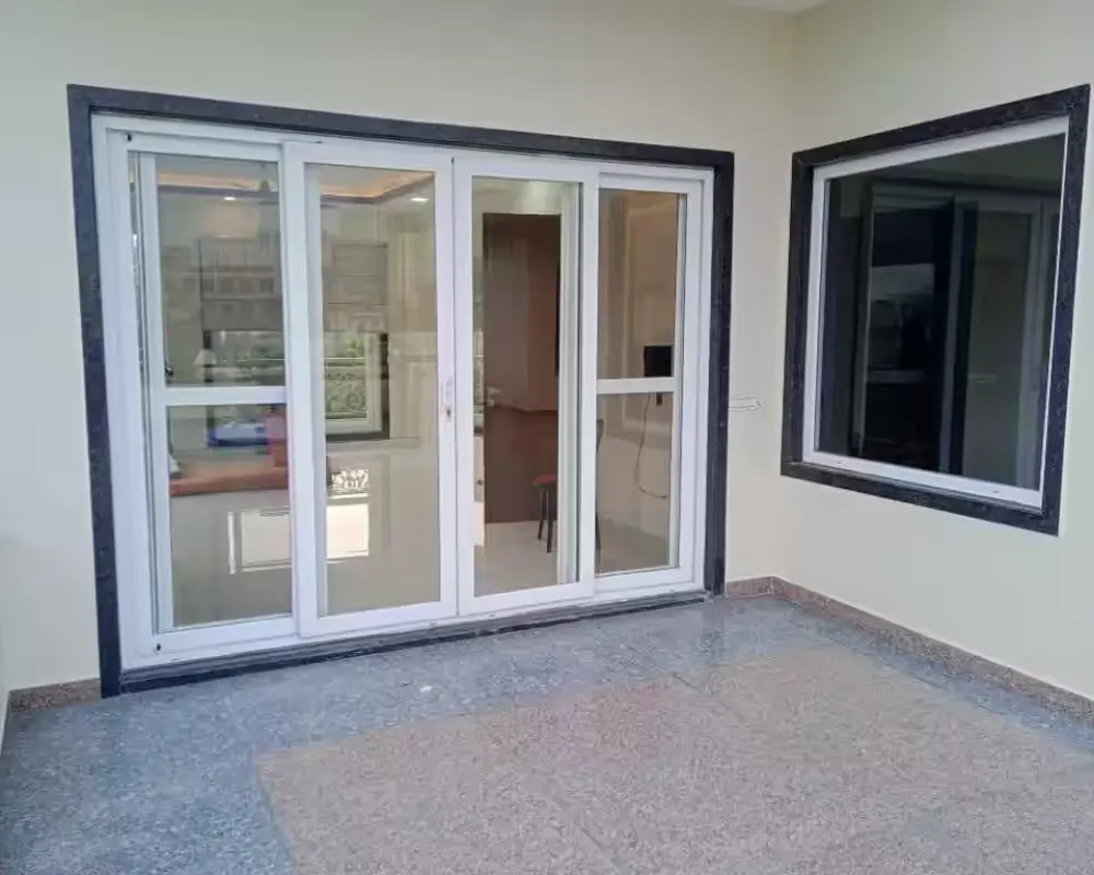 Modern residential exterior featuring a white-framed sliding glass door and large window with black trim, set against light beige walls and polished stone tile flooring.<br />