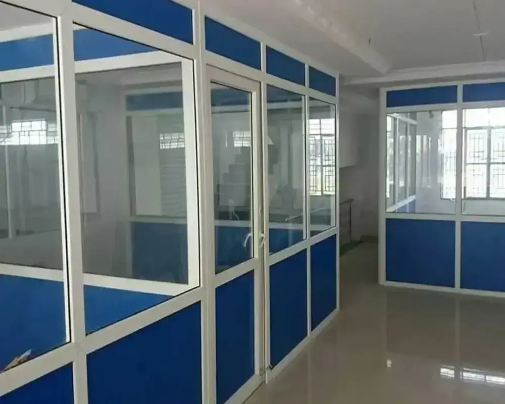 Modern office interior with glass and metal-framed partitions featuring blue panels, polished flooring, and natural light from large windows in an unoccupied space.<br />