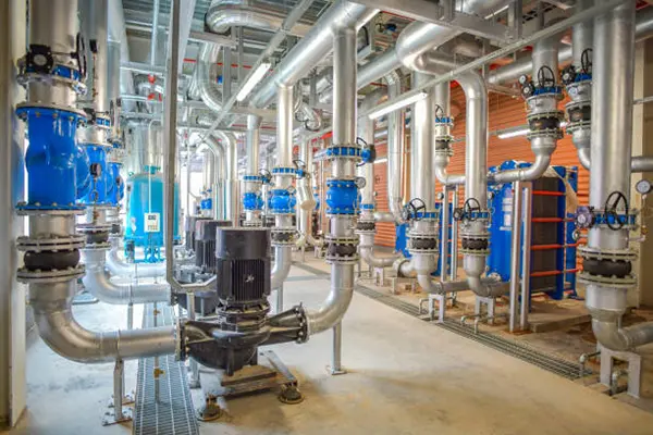 water supply & drainage system-markline qatar Industrial facility with large silver pipes, blue valves, and a central black pump, showcasing a clean and organized fluid transport system in a mechanical or water treatment setting.